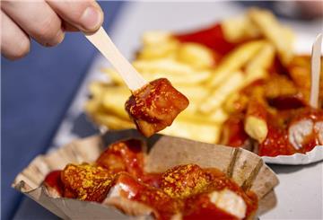 Ein Genussmoment im Zeichen der Tradition – eine Person genießt eine Currywurst zum 75. Jahrestag ihrer Erfindung. Ein kulinarisches Kulturerbe, das deutschlandweit begeistert.