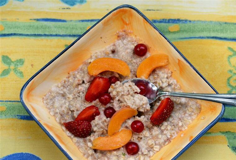Eine Schale mit Porridge und Obst steht auf einem Frühstückstisch.