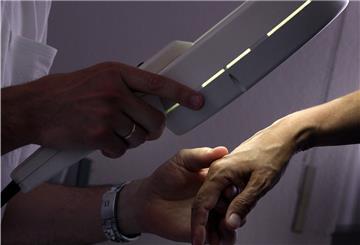 Ein Hautarzt untersucht mit einem Vergrößerungsglas die Haut einer Patientin bei einer Hautkrebs-Früherkennung.