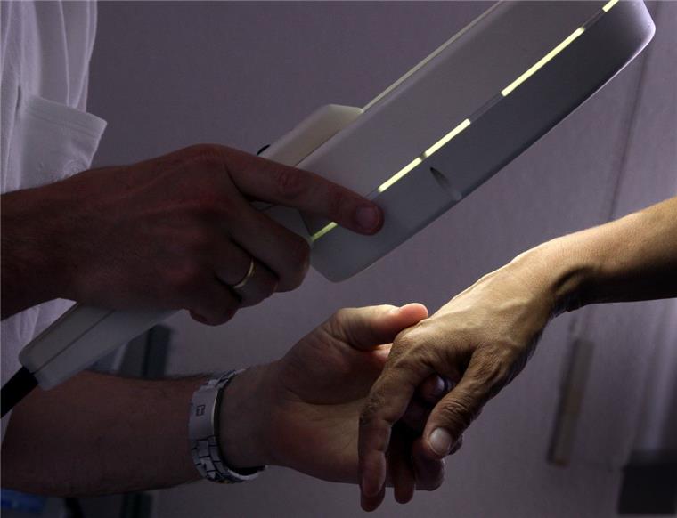 Ein Hautarzt untersucht mit einem Vergrößerungsglas eine Patientin.