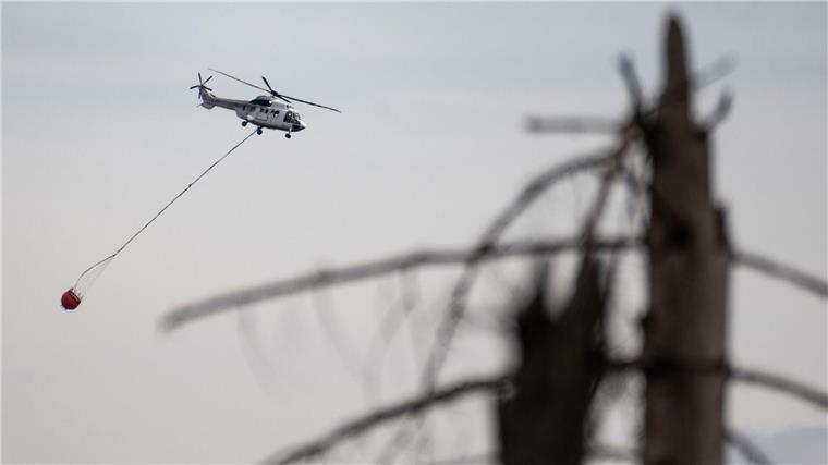 Ein Hubschrauber fliegt bei Löscharbeiten über einen Waldbrand.