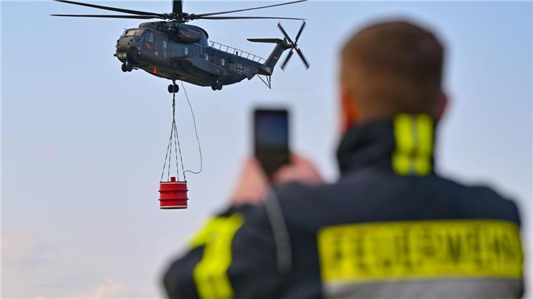 Ein Hubschrauber vom Typ Sikorsky CH-53 der Luftwaffe fliegt mit einem Wasserbehälter während einer Übung über den Flugplatz Müncheberg-Eggersdorf.