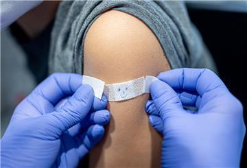 Ein JUnge lässt sich nach seiner Impfung gegen das Coronavirus ein Pflaster mit aufgemaltem Gesicht auf den Arm kleben.