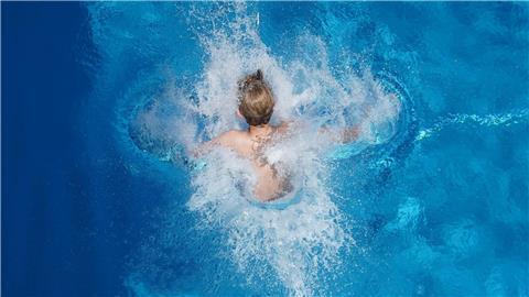 Ein Junge springt in einem Freibad ins Wasser.