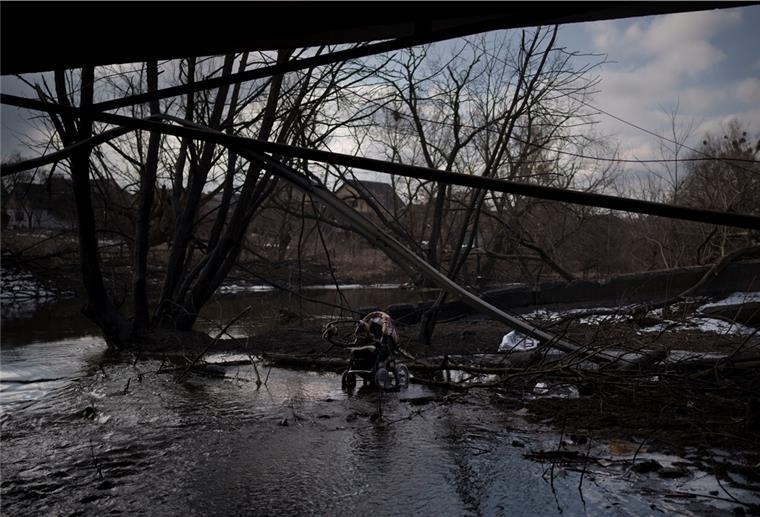 Ein Kinderwagen steht in einer Pfütze unter einer zerstörten Brücke.