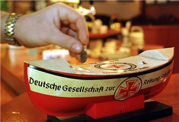 Ein Kneipen-Gast steckt eine Münze in ein Spendenschiffchen der Deutschen Gesellschaft zur Rettung Schiffbrüchiger (DGzRS).