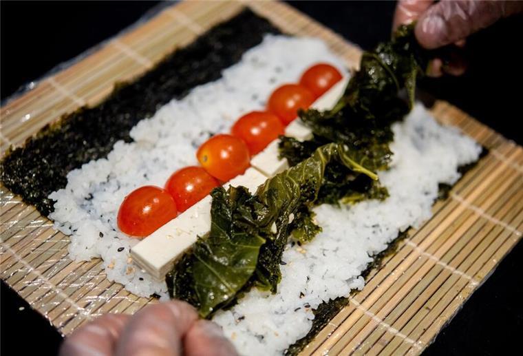 Ein Koch bereitet in der Küche des Restaurants Moto Kitchen Sushi mit Grünkohl, Tomaten und Feta zu.