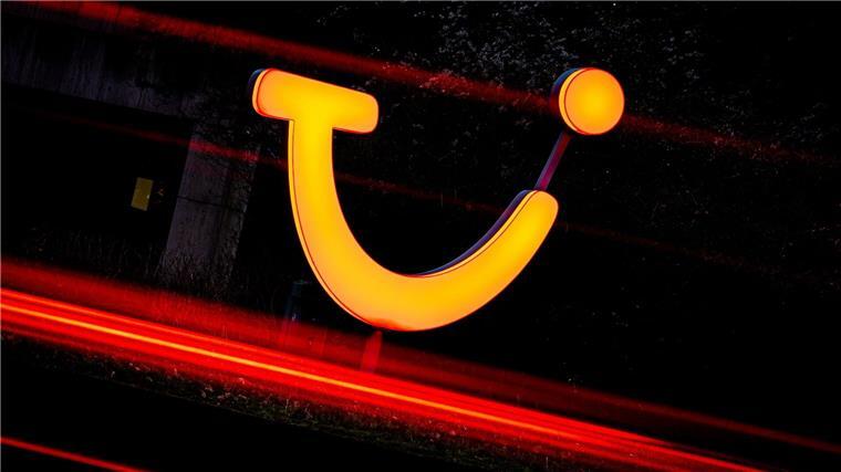 Ein Logo der Tui AG leuchtet am Morgen vor einem Gebäude der Konzernzentrale, während Fahrzeuge an dem Gebäude entlang fahren.