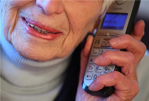  Eine Seniorin hält einen Telefonhörer an ihr Ohr. 