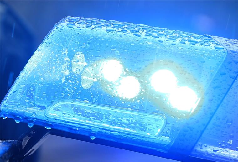 Ein Polizist steht im Regen vor einem Streifenwagen dessen Blaulicht aktiviert ist.
