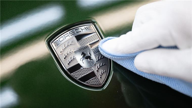 Porsche hält sich bei Jahreszielen zurück Ein Mitarbeiter der Porsche AG reinigt im Stammwerk in Zuffenhausen das Porsche-Wappen auf der Motorhaube eines vollelektrischen Porsche Taycan, nachdem er es angebracht hat.