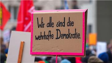 Ein Plakat „Wir alle sind die wehrhafte Demokratie“ wird auf einer Kundgebung gezeigt.
