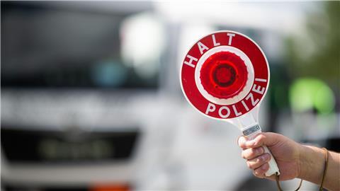 Ein Polizist hält bei einer Verkehrskontrolle eine Polizeikelle in der Hand.