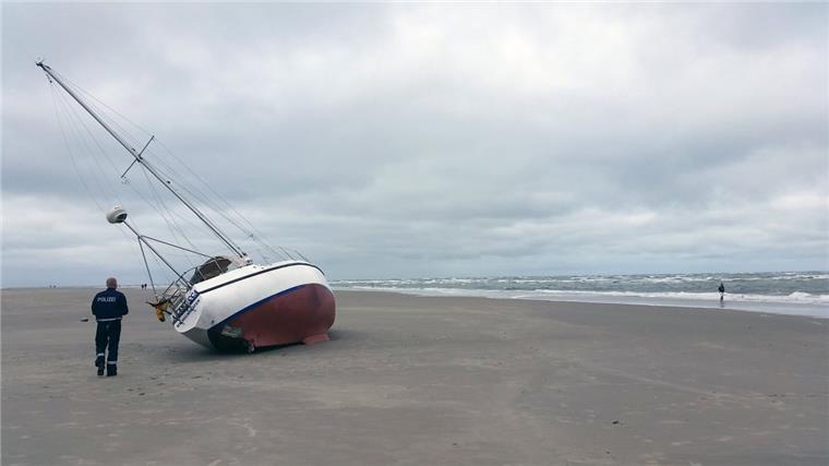 Ein Polizist steht neben dem auf Borkum gestrandeten Segelboot. 


