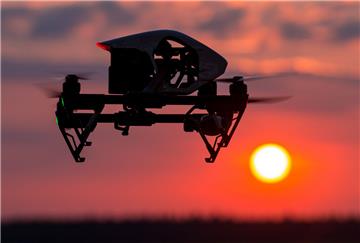 Ein Quadrocopter (Drohne) fliegt im Sonnenuntergang über einem Feld.