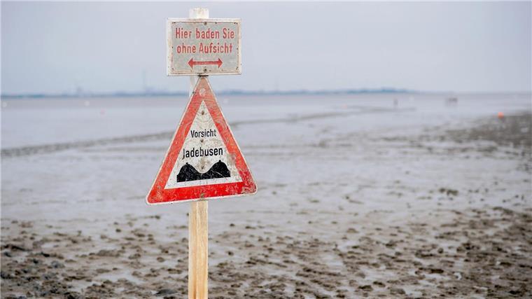 Ein Schild mit der Aufschrift „Vorsicht Jadebusen“ steht im Wattboden am Strand von Dangast.