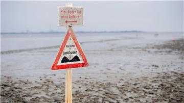 Ein Schild mit der Aufschrift „Vorsicht Jadebusen“ steht im Wattboden am Strand von Dangast.