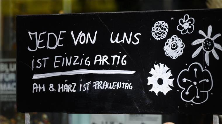 Ein Schriftzug „Jede von ist einzigartig - Am 8. März ist Frauentag“ steht auf einem Schild vor einem Blumenladen.