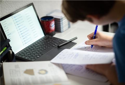 Ein Schüler sitzt in seinem Zimmer am Schreibtisch und erledigt Aufgaben im Rahmen des Homeschooling.