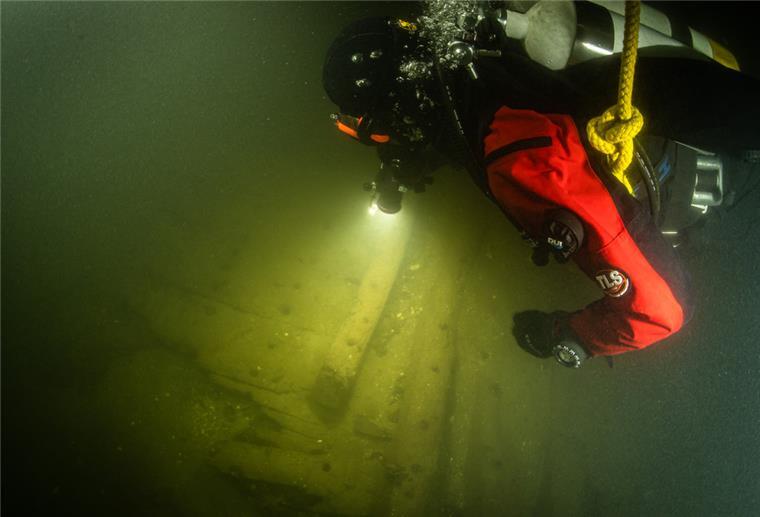 Ein Taucher benutzt in der Trave bei der Begutachtung von Planken eines Schiffswracks eine Unterwasserlampe. Taucher haben auf dem Grund der Trave ein rund 400 Jahre altes Wrack eines Hanseschiffes aus dem 17. Jahrhundert entdeckt.