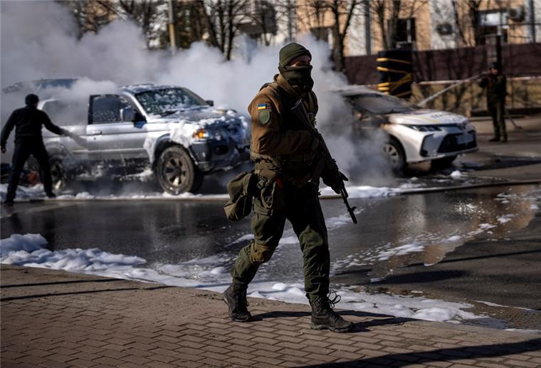 Kampf um Kiew am dritten Tag der Invasion Ein ukrainischer Soldat bezieht Stellung vor einer Militäreinrichtung, während Feuerwehrleute im Hintergrund zwei brennende Autos löschen. Russische Truppen haben den erwarteten Angriff auf die Ukraine gestartet und drangen in die Hauptstadt vor.