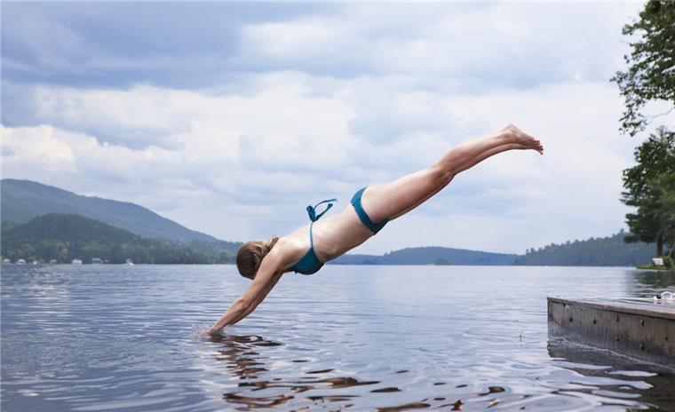 Junge Frau im blauen Bikini springt in den Spadener See der Blue Bay.