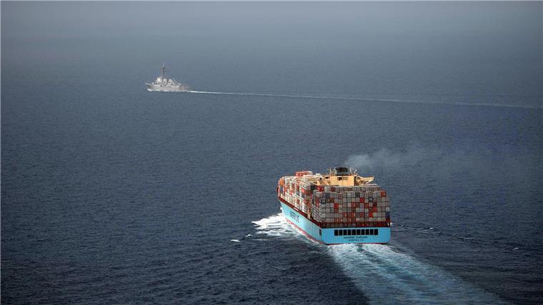 Ein US-Lenkwaffenzerstörer begleitet ein Handelsschiff, das mit Containern beladen ist.