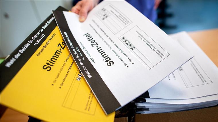 Ein Wahlhelfer gibt in einem Wahllokal die Stimmzettel für die Bürgerschaftswahl und die Kommunalwahl an die Wähler aus.