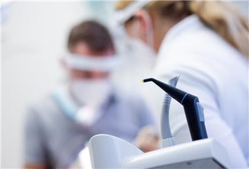 Ein Zahnarzt und eine Zahnarzthelferin mit Mund-Nasen-Schutz und Schutzvisieren versorgen eine Patientin in einer Praxis.