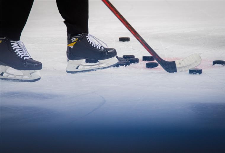 Schlittschuhe, Eishockeyschläger und Pucks liegen auf einer Eisfläche.