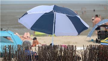 Eine ältere Frau sitzt sommerlichem am Badestrand unter ihrem Sonnenschirm.