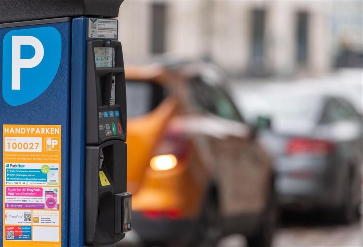 Ein Parkscheinautomat steht vor parkenden Autos.