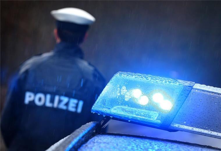 Ein Polizist steht vor einem Streifenwagen dessen Blaulicht aktiviert ist