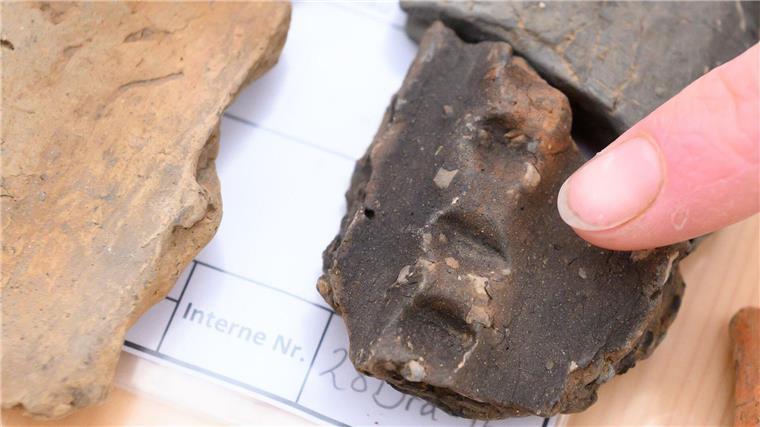 Archäologische Entdeckungen bei Bau von Stromleitung Eine Archäologin zeigt auf einen Teil von einem Fingertupfen zur Datierung der Fundstücke.
