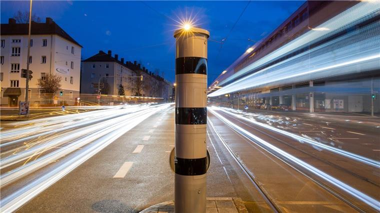 Eine Blitzsäule mit kombinierter Überwachung von Rotlicht und Geschwindigkeit steht an einer Ampelkreuzung (Langzeitbelichtung).
