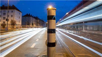 Eine Blitzsäule mit kombinierter Überwachung von Rotlicht und Geschwindigkeit steht an einer Ampelkreuzung (Langzeitbelichtung).