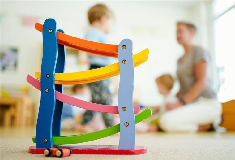 Eine Erzieherin sitzt mit Kindern hinter einer Murmelbahn und spielt. Eine erfahrene Kita-Erzieherin berichtet über ihre Red-Flags in Kindertagessstätten.