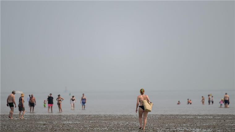 Eine Frau geht bei sommerlichen Temperaturen am Nordseestrand von Schillig im Watt auf andere Strandgäste zu, die teilweise im Wasser sind.