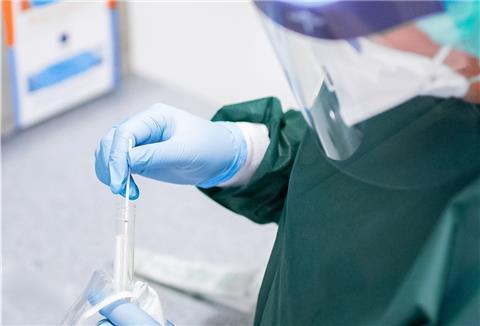 Eine Frau in Schutzkleidung packt ein Abstrichröhrchen aus.