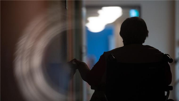 Eine Frau sitzt in einem Alten- und Pflegeheim in einem Rollstuhl auf einem Gang.