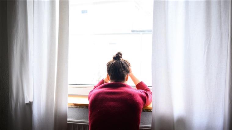 Neues Online-Angebot für Mütter mit Depressionen nach Geburt Eine Frau sitzt mit Kopf in den Händen am Fenster.