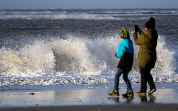 Sturm über der Nordsee - Fähre fällt aus Eine Frau steht mit einem Kind am Strand vor den tosenden Wellen der Nordsee.
