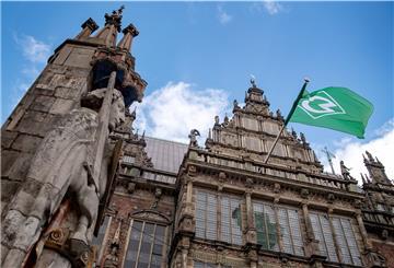 Eine ganze Stadt zeigt Flagge: Das Wahrzeichen Bremer Roland steht vor dem Rathaus, an dem die Flagge von Werder Bremen hängt. 