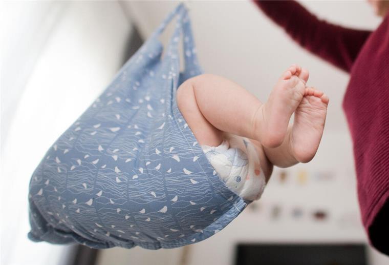 Eine Hebamme wiegt im Rahmen der Nachsorge ein Baby.
