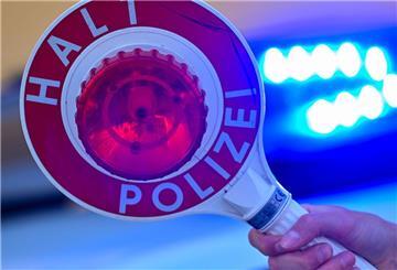 Eine Kelle der Polizei mit der Aufschrift Halt Polizei vor einem Blaulicht eines Polizeifahrzeuges (Symbolbild)