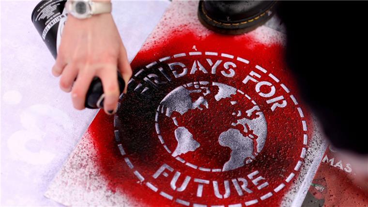 Eine Klimaaktivistin sprüht ein „Fridays For Future“-Logo auf ein Transparent.