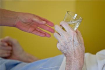 Eine Krankenpflegerin reicht einem Patienten in ein Glas Wasser.