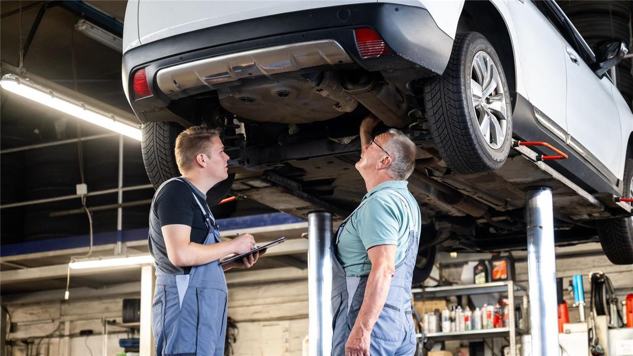 Zwei Männer in einer Autowerkstatt unter einem Auto 