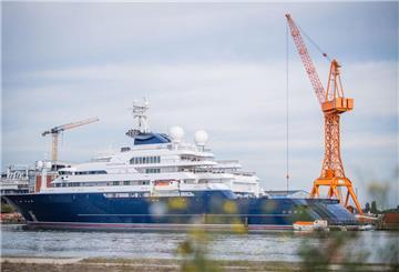 Eine riesige Yacht liegt im Hafen. Im Hintergrund sind Kräne zu sehen.