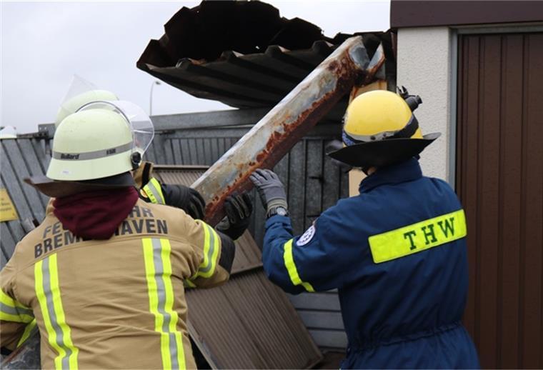 Zwei Feuerwehrmänner stehen vor einer demolierten Garage und manövrieren ein Stück Metall.